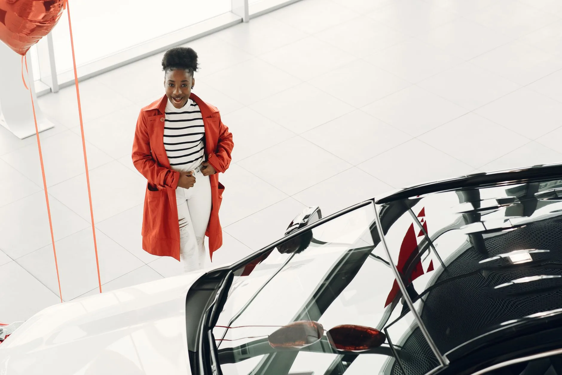 Uśmiechnięta kobieta w czerwonym płaszczu ogląda sportowe auto w salonie